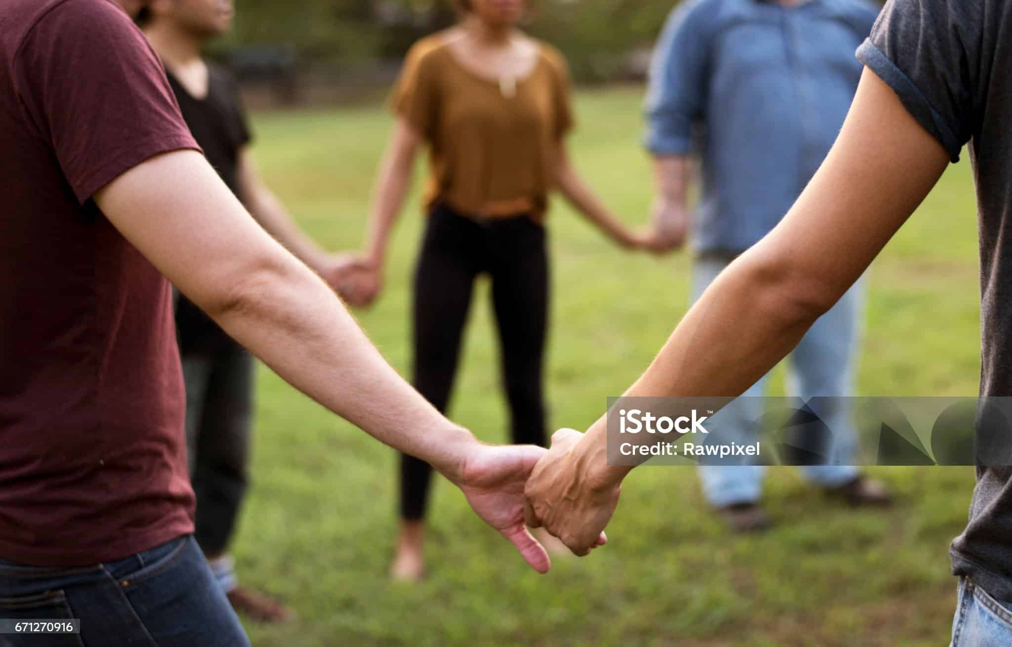 Un groupe de personnes debout en cercle dans l’herbe, se tenant par la main